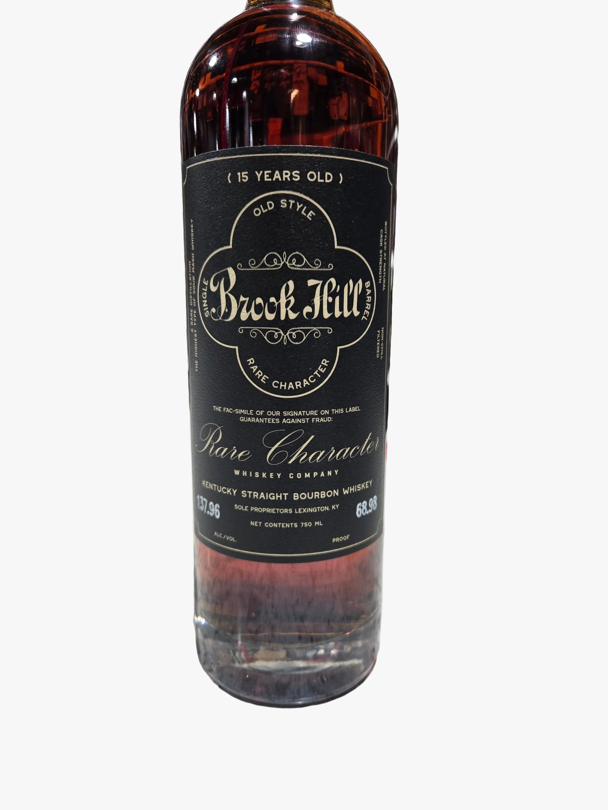 A bottle of Brock Mill Pure Character 15 Years Old bourbon whiskey standing on a speckled countertop with a blurred liquor store shelf in the background.