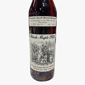 A bottle of Black Maple Hill bourbon whiskey on a speckled stone countertop in a liquor store, with a blurred background of shelves and bottles.
