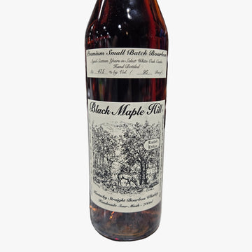 A bottle of Black Maple Hill bourbon whiskey on a speckled stone countertop in a liquor store, with a blurred background of shelves and bottles.