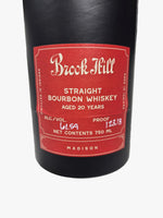 A close-up of a Buck Feill Straight Bourbon Whiskey bottle, showing the black glass body and a red label with white text, resting on a gray marble surface.