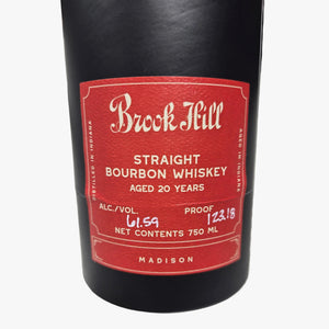 A close-up of a Buck Feill Straight Bourbon Whiskey bottle, showing the black glass body and a red label with white text, resting on a gray marble surface.
