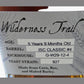A close-up of a whiskey bottle with amber liquid and a white label reading Wilderness Trail, showing details like age, barrel, and yeast strain.