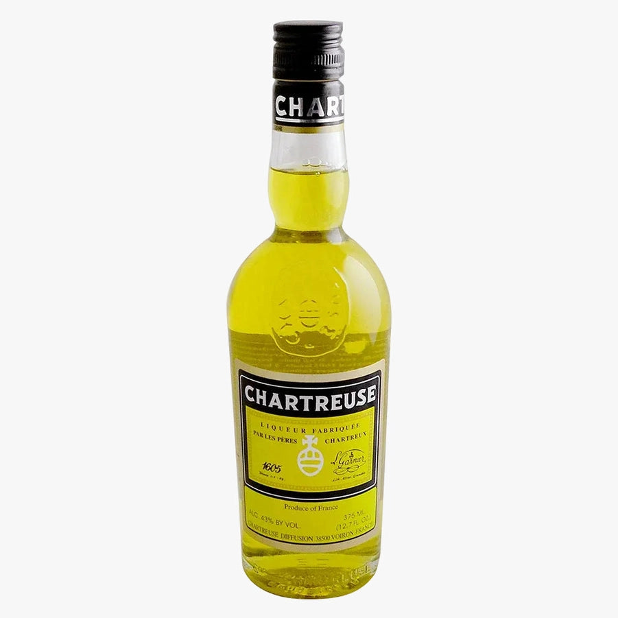 A bottle of Chartreuse liqueur with a black cap and a yellow-green liquid inside a clear glass bottle, shown against a plain white background.