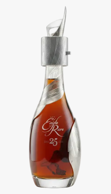 A luxury bottle of cognac with a sculptural clear glass body, etched silver details, and a silver pour spout. The amber liquid inside is labeled 'An Eagle Rare 25 Anvil Edition'.