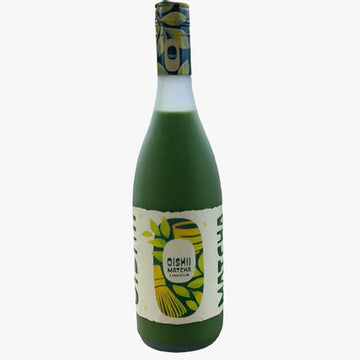 Two green glass bottles of Oishii Matcha Green Tea liquid with cream and yellow labels, standing on a wooden table with a blurred outdoor background.